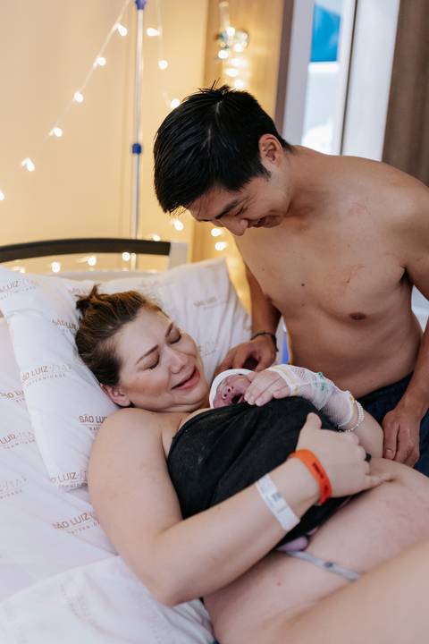 Foto do casal emocionado recebendo a bebê nos braços logo após o parto.'