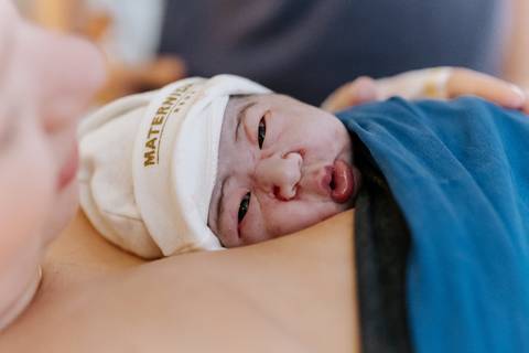 Foto aproximada da bebê olhando para a câmera no colo materno.'