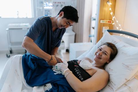 Foto do casal trocando carinhos enquanto seguram a bebê.'