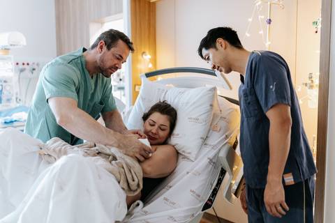 Foto da equipe médica auxiliando a mãe com a bebê recém-nascida.'