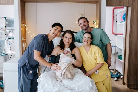 Foto da equipe médica posando com a família na sala de parto.'