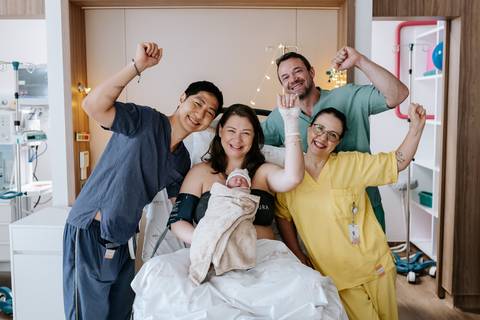 Foto da família e equipe vibrando com braços erguidos em comemoração.'