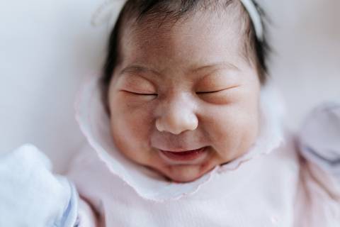 Foto aproximada do rosto da recém-nascida esboçando um sorriso.'