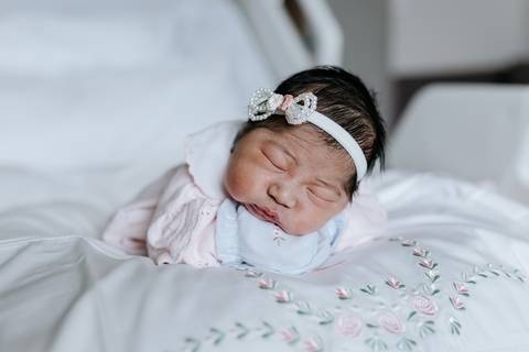 Foto da bebê dormindo calmamente com laço na cabeça.'