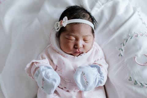 Foto da bebê enrolada em manta rosa com luvas combinando.'