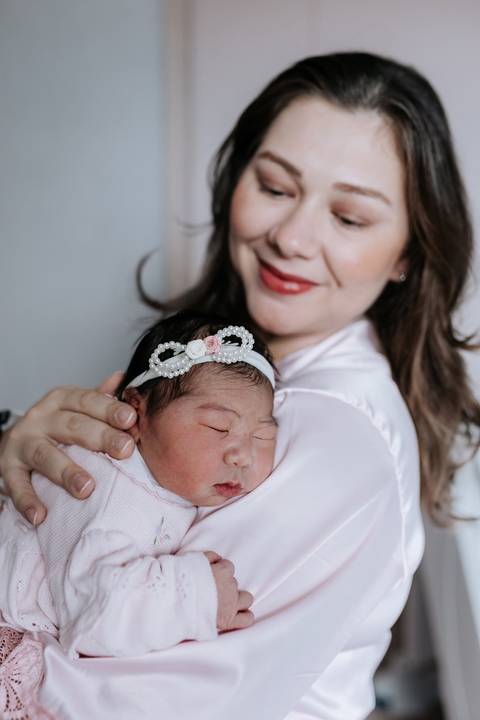 Foto aproximada da mãe abraçando a bebê com ternura.'