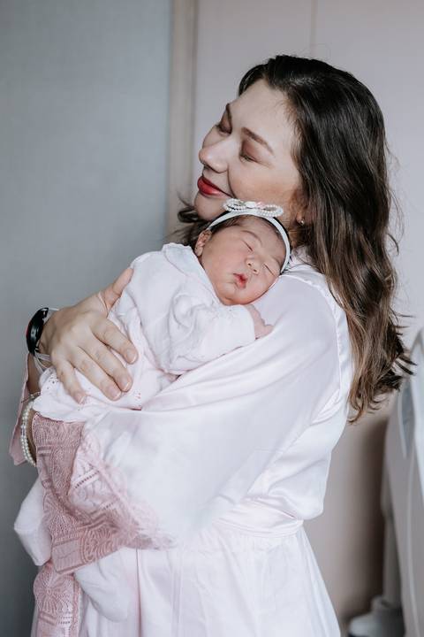 Foto da mãe amparando a bebê dormindo contra o peito.'