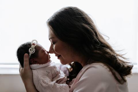 Foto em silhueta da mãe aproximando o rosto da bebê.'