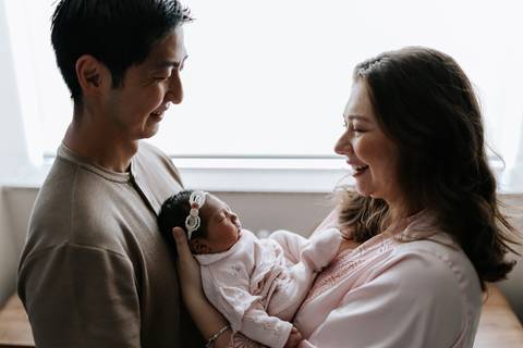 Foto do casal observando a recém-nascida sob luz de contra-janela.'
