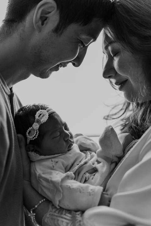 Foto em preto e branco do casal e bebê em momento íntimo.'