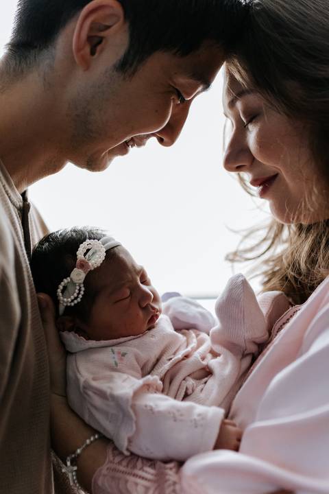 Foto de detalhe do casal admirando a expressão da recém-nascida.'