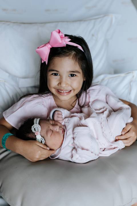Foto da irmã mais velha sorrindo com a bebê no colo.'