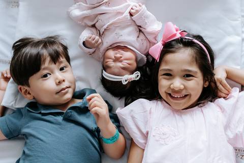 Foto dos três irmãos deitados juntos na cama da maternidade.'