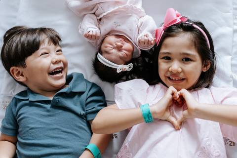 Foto dos irmãos sorrindo e fazendo um coração com as mãos.'