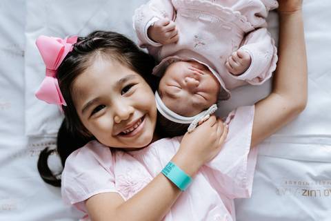 Foto aproximada da irmã mais velha abraçada à bebê.'