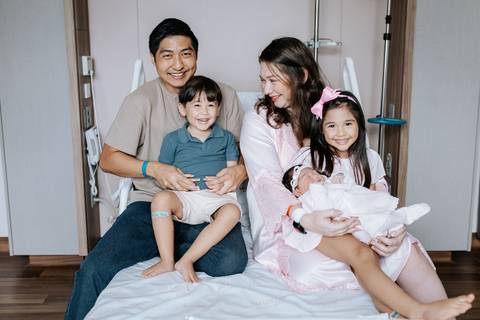 Foto do casal com os três filhos em momento de celebração no hospital.'