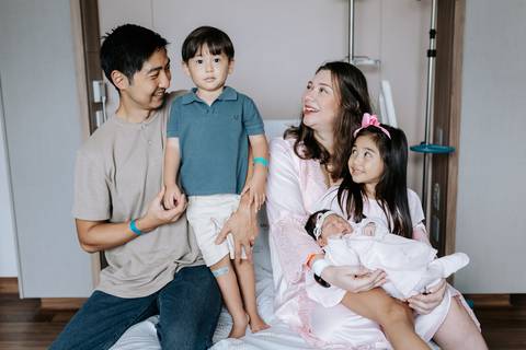 Foto da família trocando olhares carinhosos com a bebê recém-nascida.'