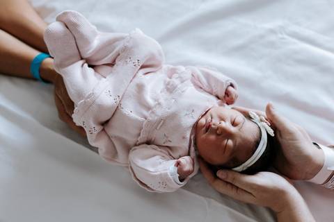 Foto das mãos dos pais segurando a bebê. '