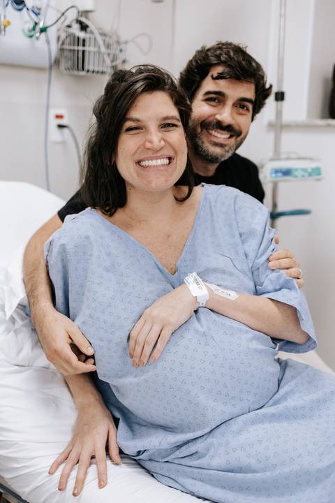 Foto aproximada da gestante sorrindo com as mãos na barriga antes do parto.'