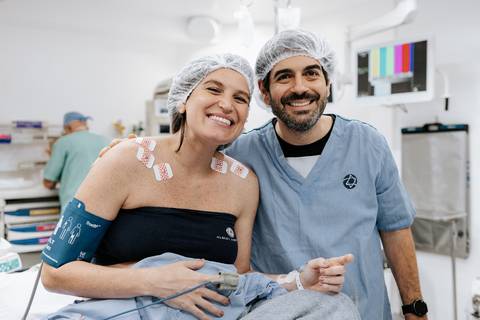 Foto do casal sorrindo e abraçado já paramentados para o centro cirúrgico.'