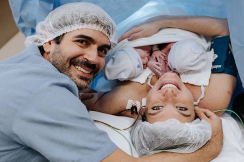 Foto do casal radiante com os dois bebês próximos aos seus rostos.'