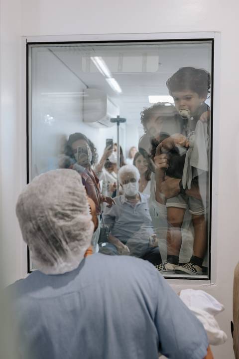 Foto da família e amigos emocionados observando os bebês através do vidro.'