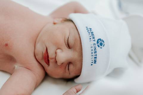 Foto de close do rosto de um dos gêmeos dormindo com touca hospitalar.'