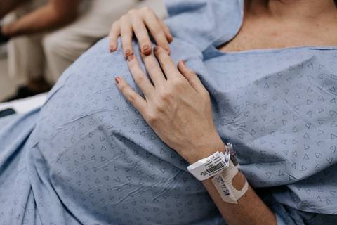 Foto em detalhe da mão da gestante sobre a barriga.'