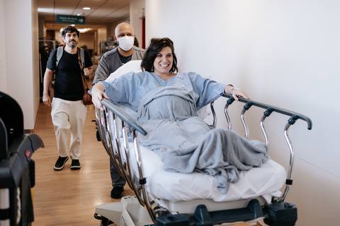 Foto da gestante sendo levada na maca enquanto sorri para a câmera.'