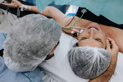 Foto aproximada da mãe recebendo carinho no rosto durante o parto.'