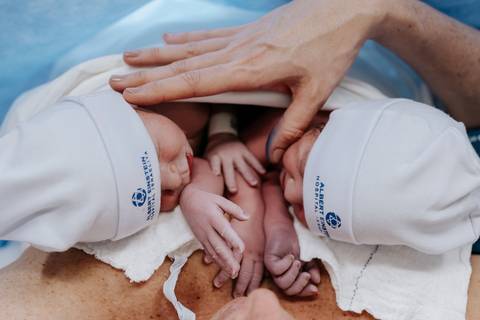 Foto das mãos da mãe amparando os dois bebês no colo.'