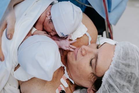 Foto aproximada da mãe acolhendo os gêmeos com ternura.'