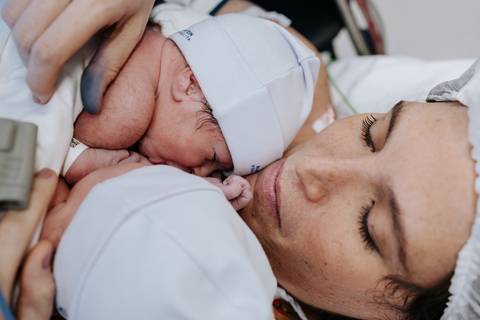 Foto da mãe com os olhos fechados aproveitando o contato pele a pele duplo.'