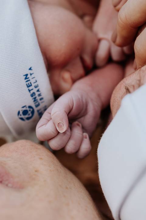 Foto em detalhe da mão de um dos bebês segurando o dedo da mãe.'