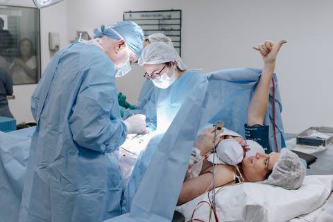Foto da mãe dando sinal de positivo para a família que estava assistindo o parto do vidro. '