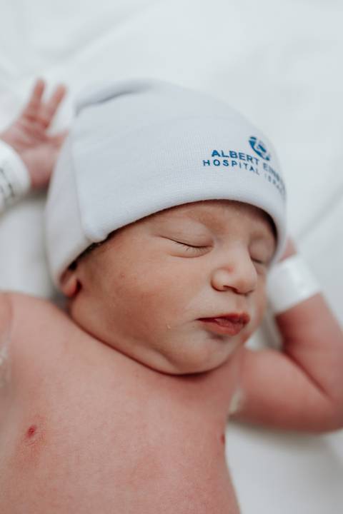 Foto de perfil do recém-nascido com touca da maternidade.'