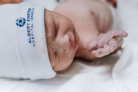 Foto de close do rosto do bebê com touca da maternidade.'