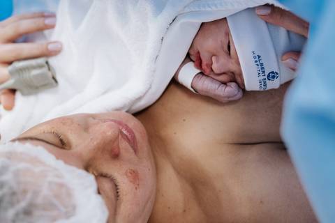 Foto da mãe olhando e sentindo o contato pele a pele com o filho.'