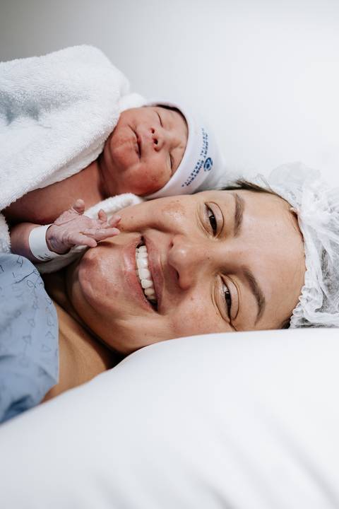 Foto da mãe radiante sorrindo com o bebê próximo ao seu rosto.'