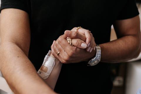 Foto em detalhe das mãos do casal entrelaçadas em apoio.'