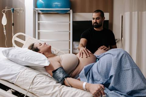 Foto do parceiro com a mão sobre a barriga da gestante.'