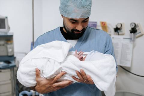 Foto do pai segurando a bebê no colo com olhar de proteção.'