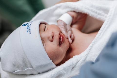 Close do bebê recém-nascido envolto em manta branca sorrindo.'