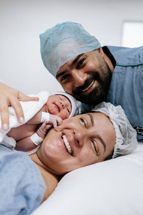 Retrato do casal sorrindo com o pequeno no colo, próximo ao rosto da mãe.'