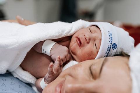 Foto aproximada da mãe abraçando o filho com ternura no pós-parto.'