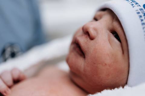 Close do rosto do bebê com foco no olhar e na touca da maternidade.'