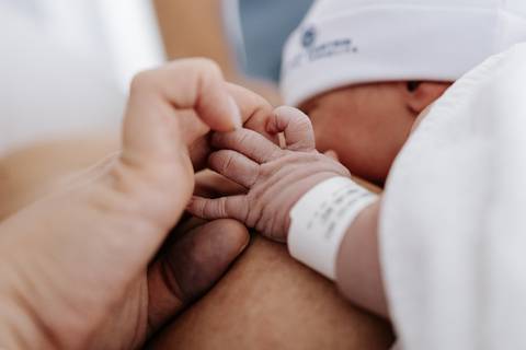 Detalhe das mãozinhas do bebê segurando o dedo da mãe no primeiro contato.'