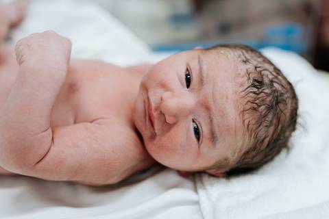 Recém-nascido deitado no berço logo após os primeiros cuidados.'