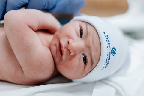 Close do rosto do bebê com touca azul da maternidade.'