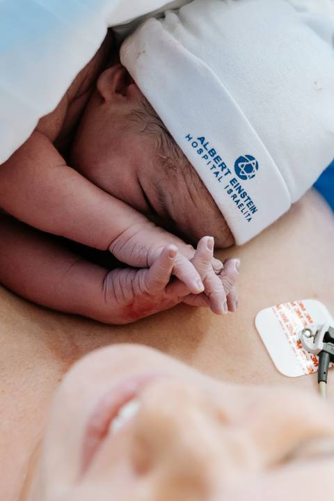 Detalhe das mãos do bebê em contato pele a pele com a mãe.'